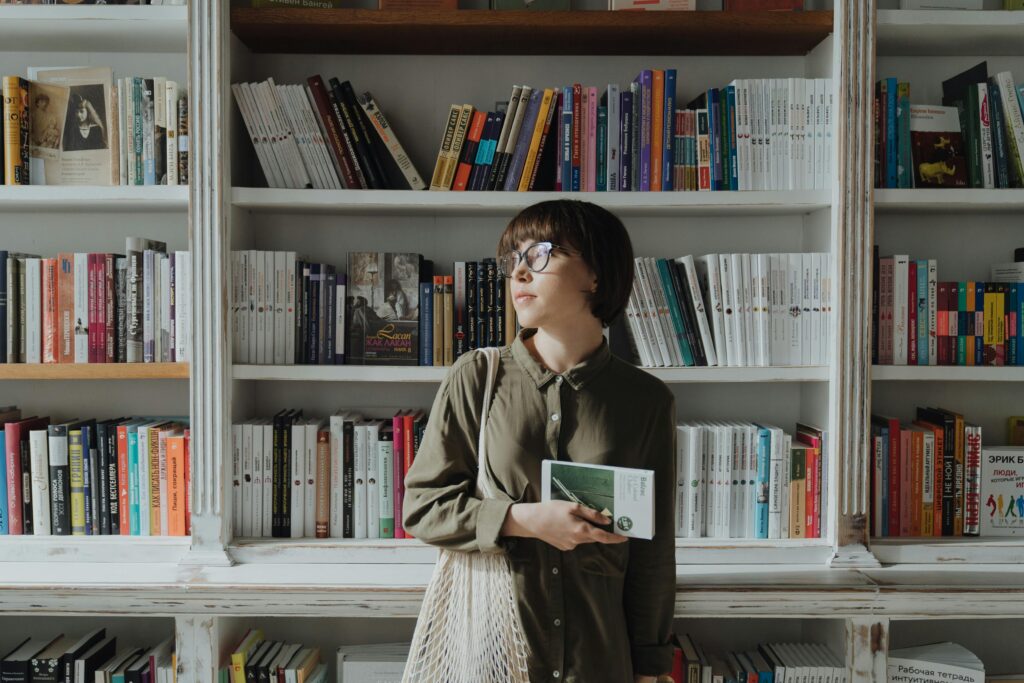 Pessoa estudando em biblioteca, cercada por livros, representando a curiosidade intelectual e a expansão da mente.